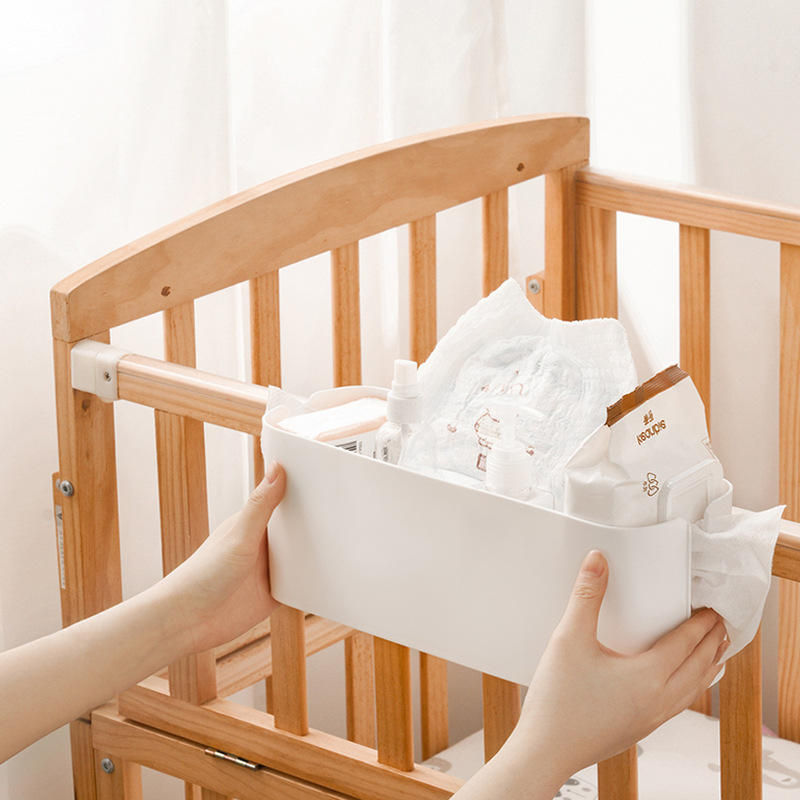 White hanging storage basket being installed on wooden baby crib