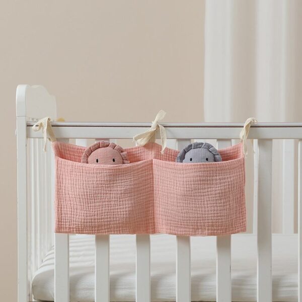 Pink fabric hanging storage basket attached to baby crib rail