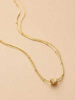 Gold layered bar chain necklace on beige background