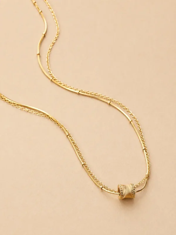 Gold layered bar chain necklace on beige background