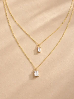 Gold layered baguette crystal necklace on beige background