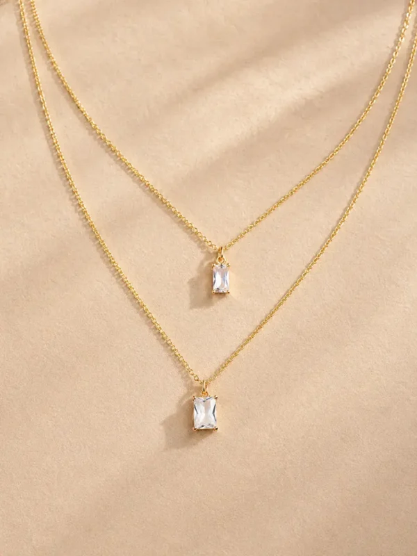 Gold layered baguette crystal necklace on beige background