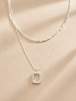 Silver layered rectangle pendant necklace set on beige background
