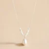 Silver-tone pearl drop necklace on beige background