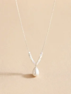 Silver-tone pearl drop necklace on beige background