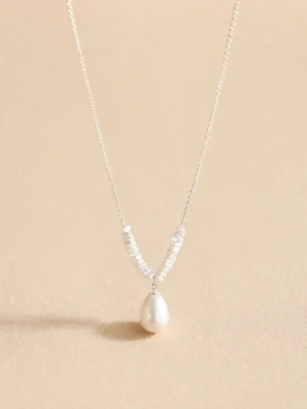 Silver-tone pearl drop necklace on beige background